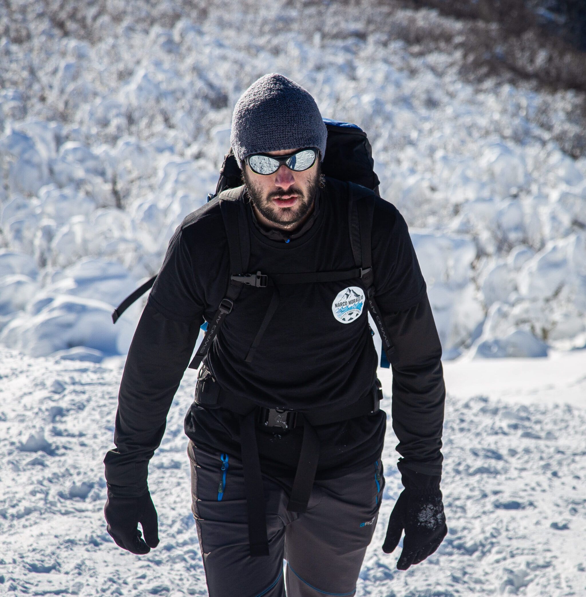 Marco Moraglio in salita su neve, occhiali da ghiacciaio e zaino.